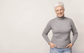 older woman with hands in pockets smiling on a toupe background