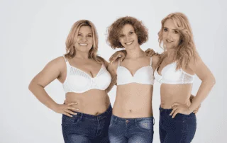 Three confident women in jeans and bras smiling and embracing
